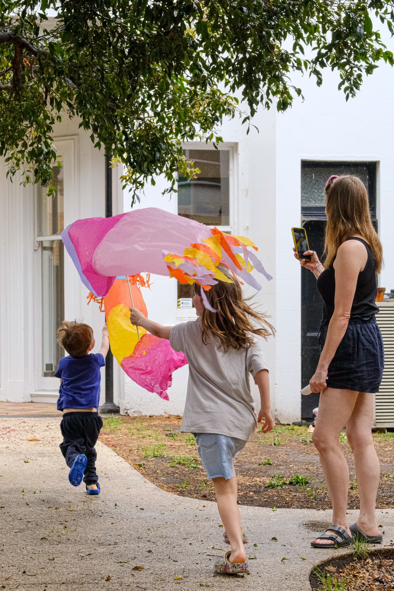 Children running outdoors with a large colourful tissue-paper tube kite flying behind them